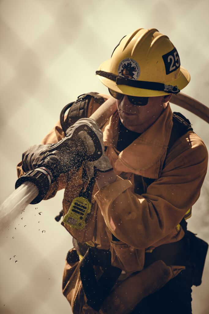 Firefighter in action with hose spraying water.