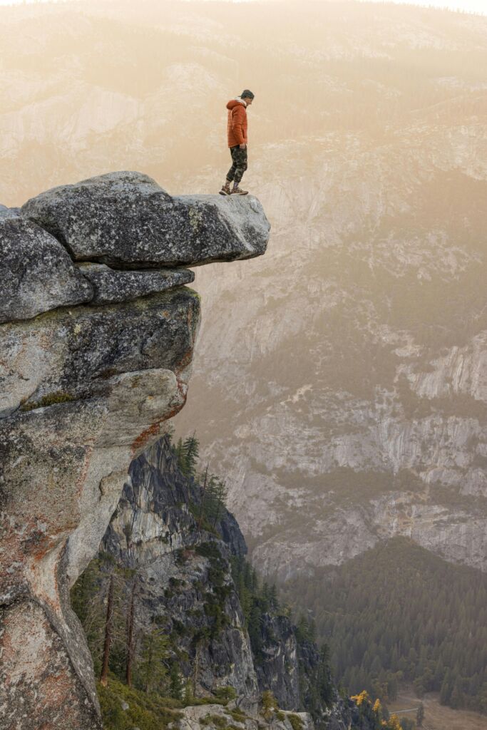 Person standing on cliff edge, overlooking mountainous view.