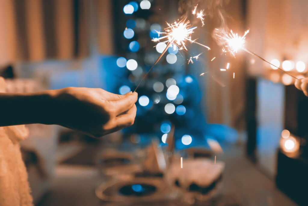 Hands holding sparklers, festive bokeh lights.