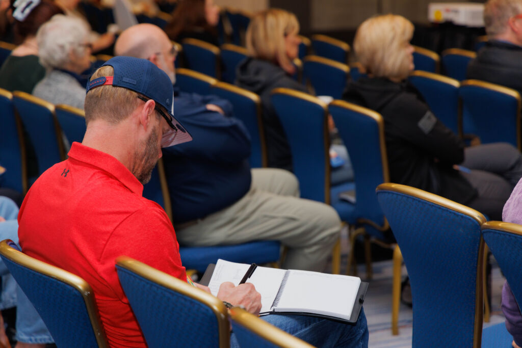 Attendees sitting, man in red taking notes.